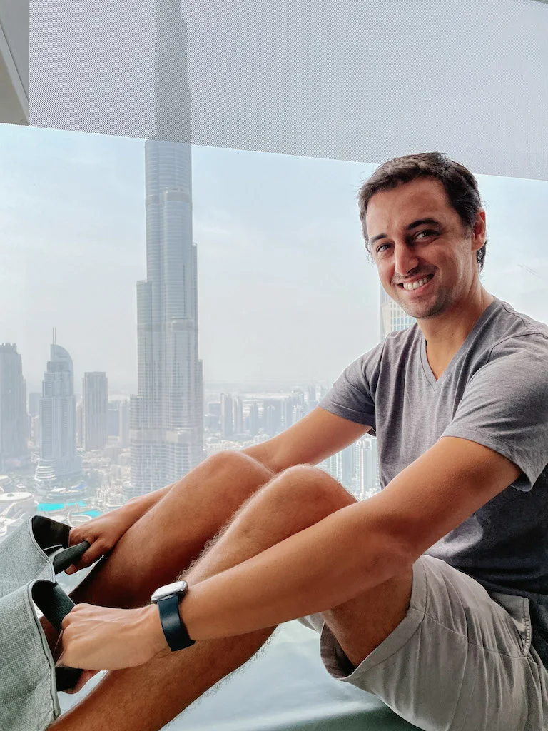 A man sitting at the top of a Glass Slide with the city behind him