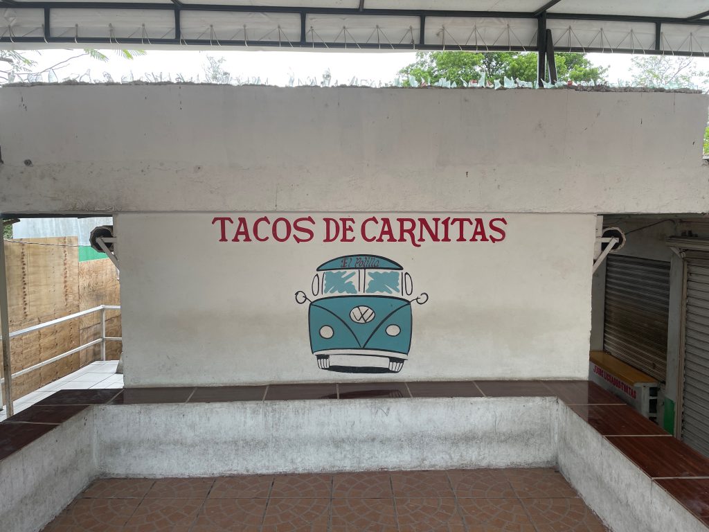 A white wall with a sign that reads Tacos de Carnitas, and a blue van drawn on it