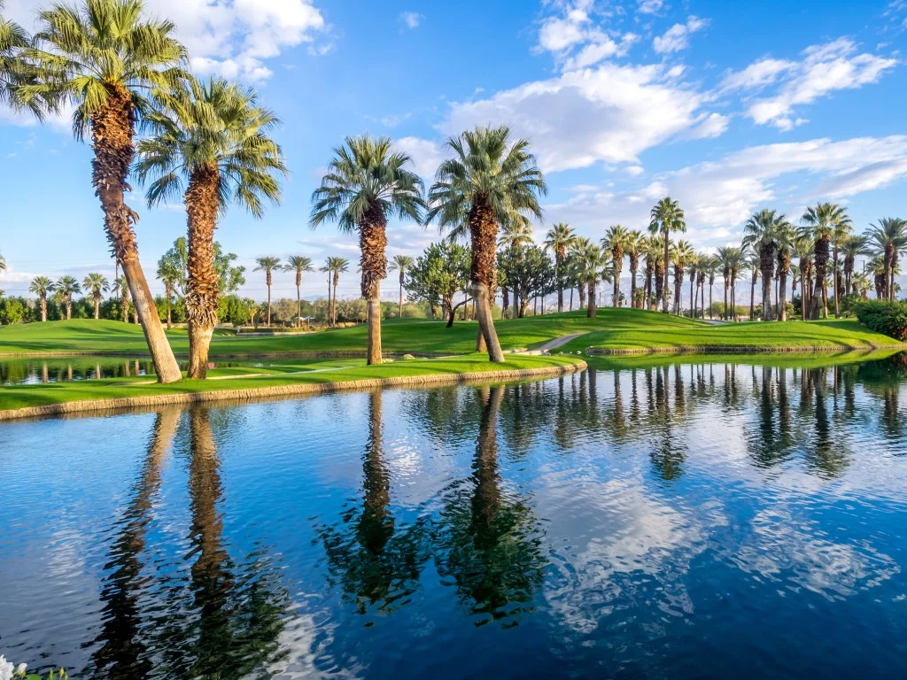 Image of a golf course by a lake, dotted with palm trees in Palm Desert, one of the best day trips from Palm Springs destinations 