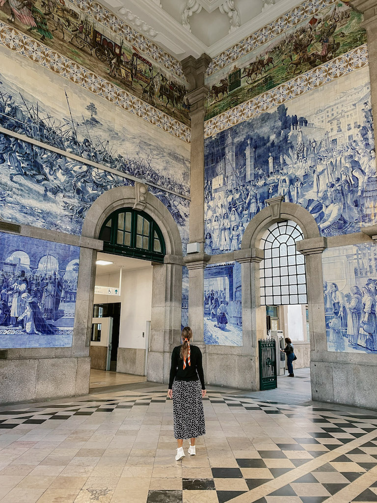 Image of the interior of a train station covered in azulejo tiles with images that tell the story of Portugal. It's Sao Bento Station, a must-visit while spending one day in Porto