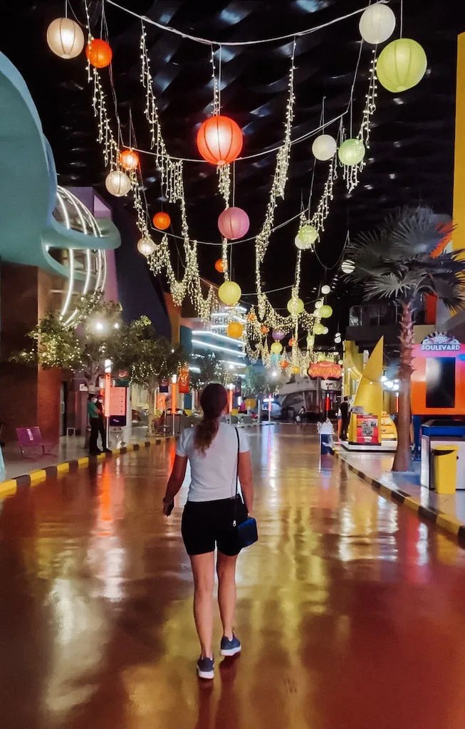 A woman walking along a road with fairy lights hanging above her