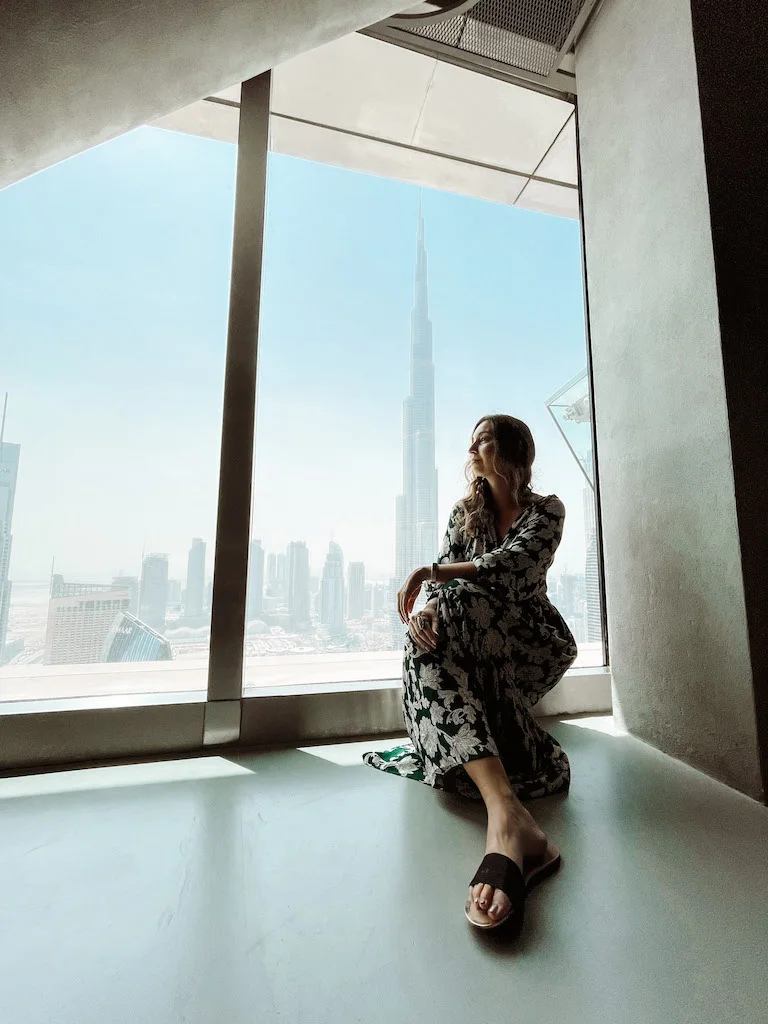 A woman sitting next to a window overlooking the Burj Khalifa