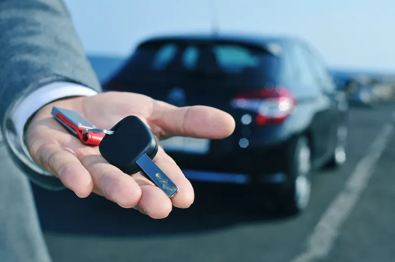 Image of a hand holding a car key, with a black car parked in the background