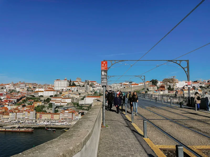 People crossing the Dom Luis I Bridge, with the city of Porto in the background 