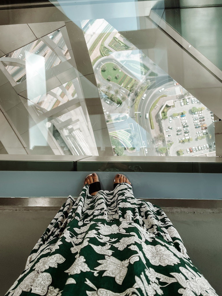 A woman's feet standing on a glass bridge, looking at the city below her