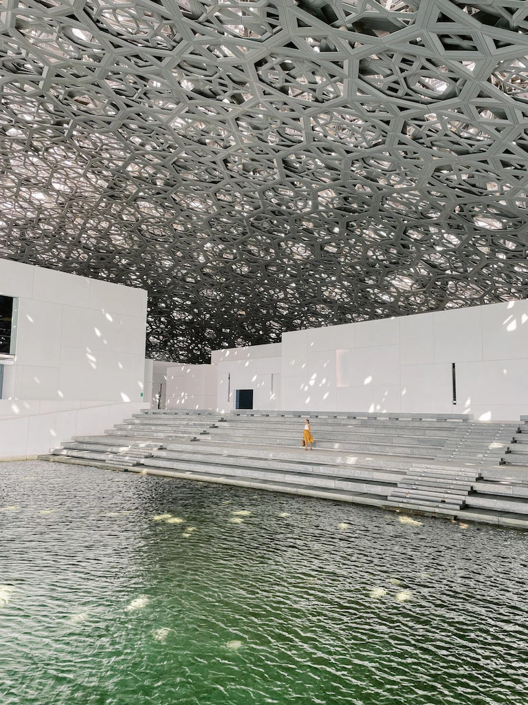 A woman standing on the steps that lead to the canals in Louvre Abu Dhabi