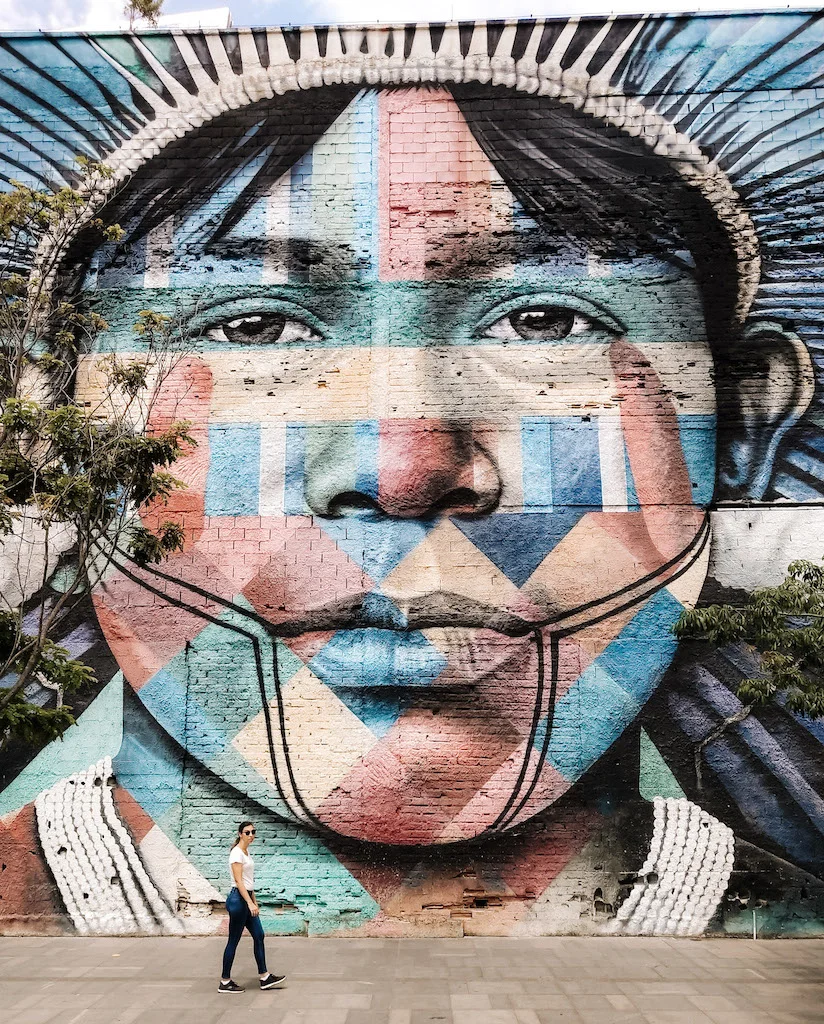 A woman walking in front of a very large mural of a  boy