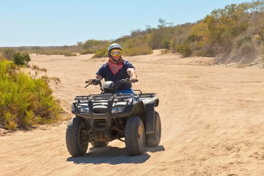 A man with a helmet driving an ATV on a sand road.