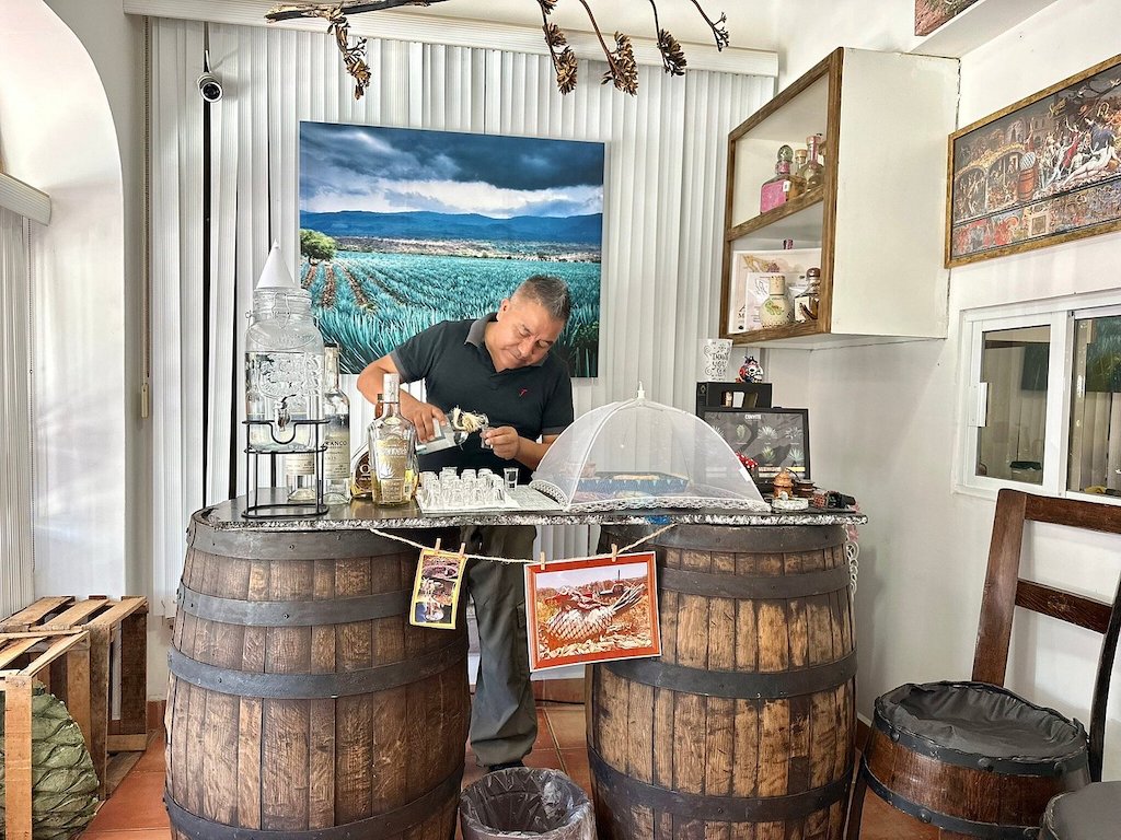 Man behind a table pouring tequila into shot glasses.