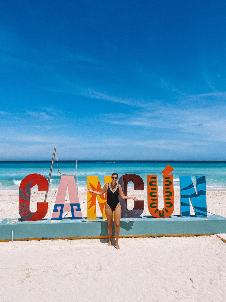 A woman in a black swimsuit posing in front of the Cancun sign