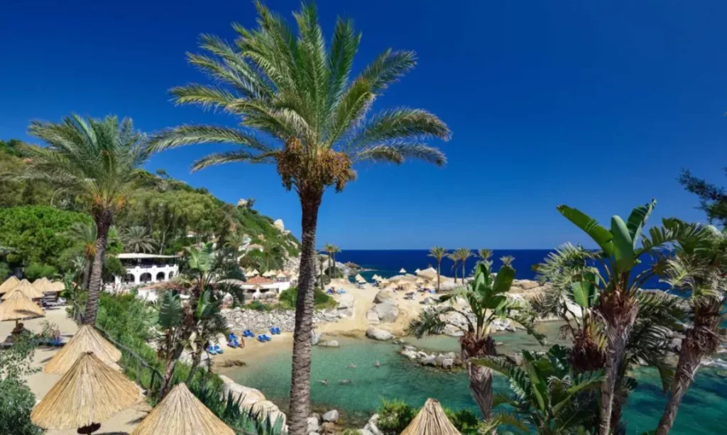 Image of the green areas of Arbatax Park Resort, with palm trees, swimming pools, and the sea in the background