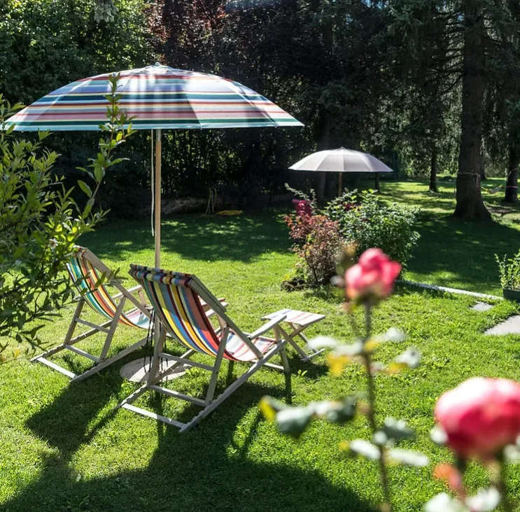 Image of a garden with green grass, two sun chairs and sun umbrellas, and roses at one of the best eco resorts in Italy