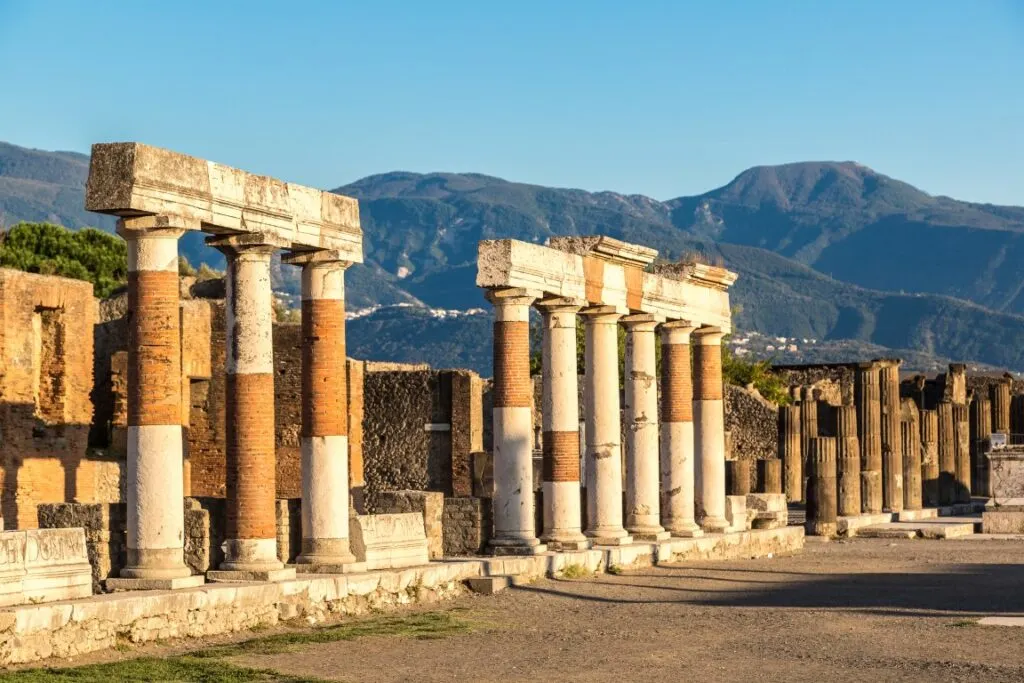 Ruins of two sets of columns in Pompeii, one of the best day trips from Naples, with hills in the background