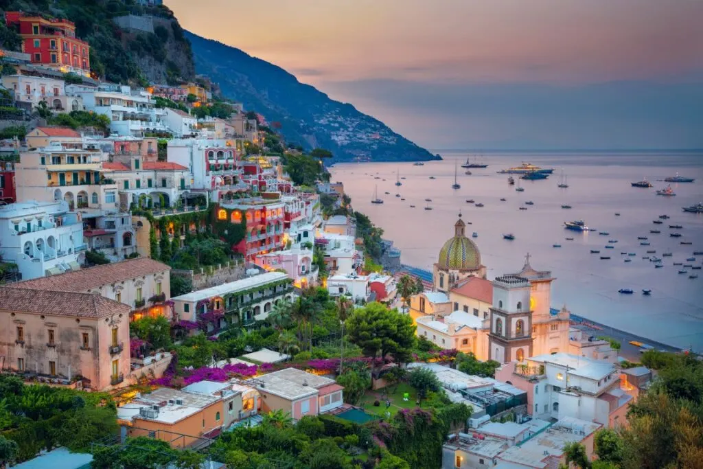 Image of Positano during sunset, with the cliff-perched houses lit up. Inserted in a post about Sorrento vs Positano vs Amalfi 