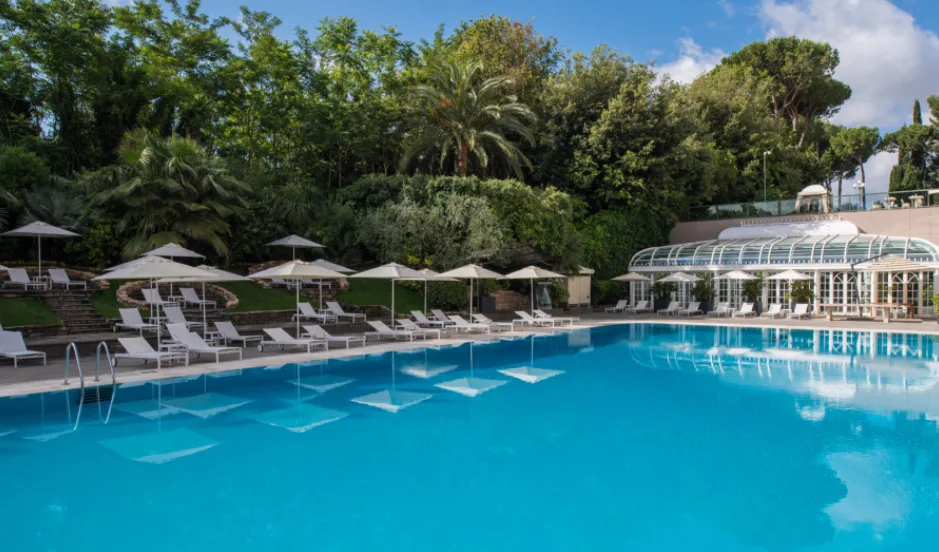 A large swimming pool surrounded by white sun loungers and umbrellas