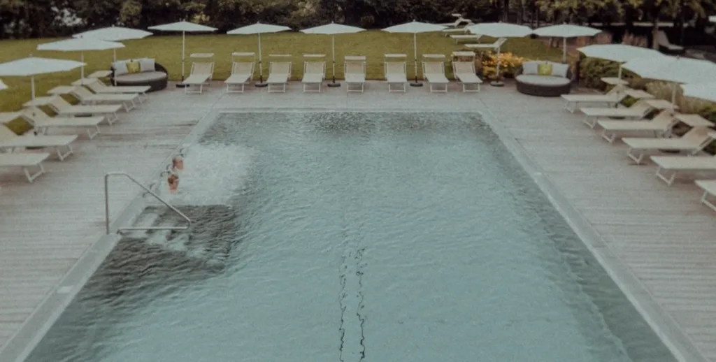 Image of a swimming pool surrounded by sun loungers and sun umbrellas, inserted in a post about the best eco resorts in Italy