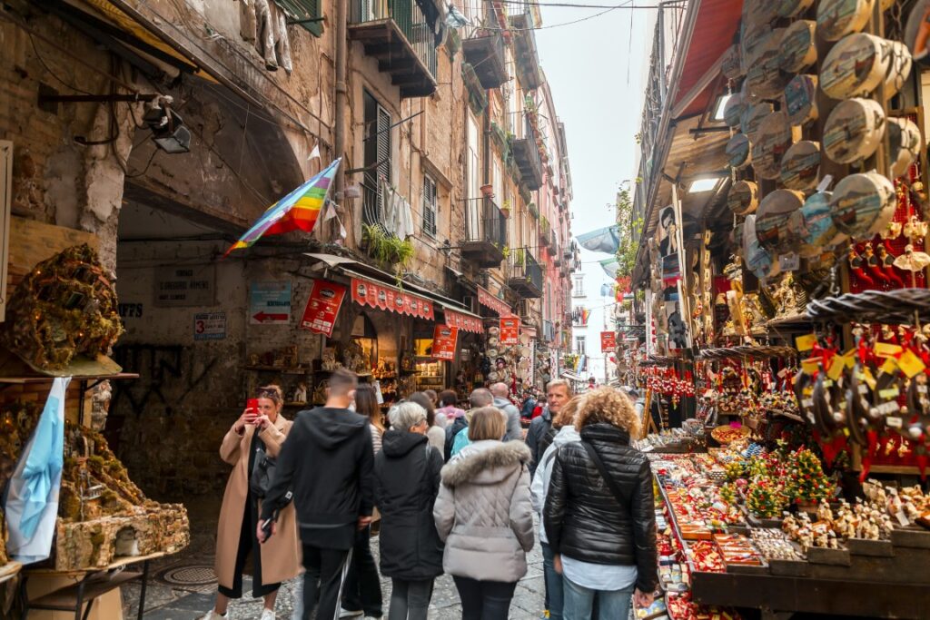 Image of a narrow street lined by shops on both sides featuring stalls full of Christmas ornaments, and tourists walking along, one of the best things to do in Naples