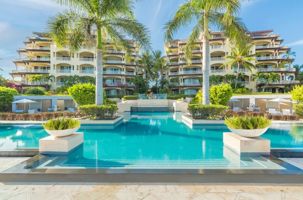 A very bright image of a resort in the background, two palm trees in the center and a large swimming pool in the foreground, inserted in a post about the best eco resorts in the Caribbean