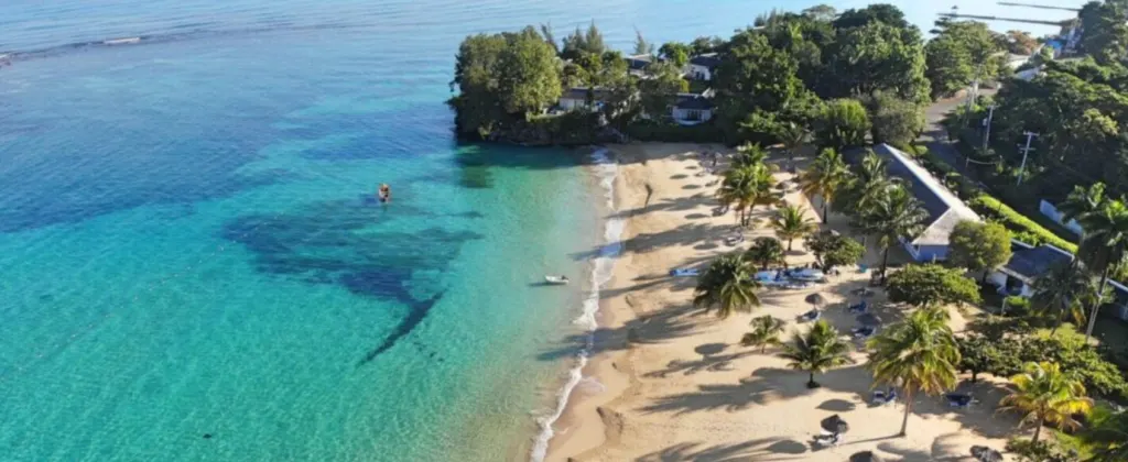 In this image the turquoise Caribbean Sea can be seen on the left, and the beach on the right, with some palm trees and other vegetation