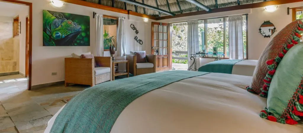 Image of a hotel room with two double beds, two sofas against a wall, and an open door that lets in light