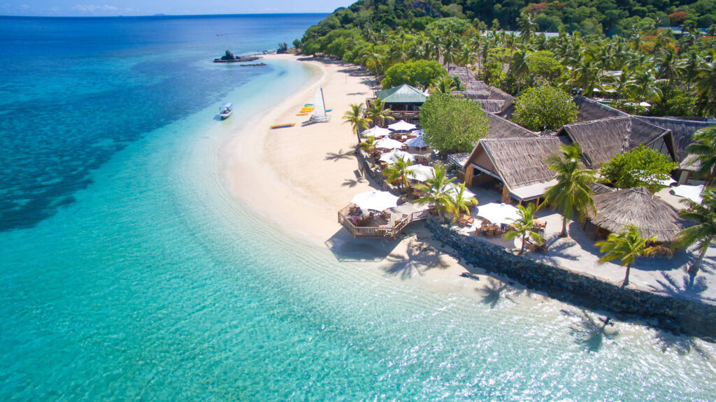 Turquoise waters, a pristine shoreline and resort cabins surrounded by palm trees. 