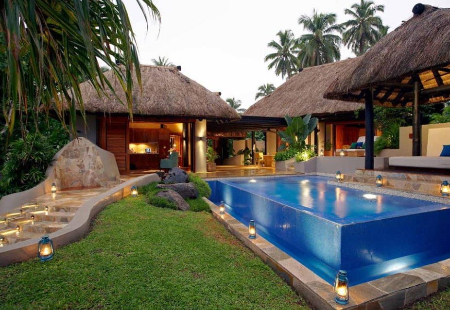 A couple of resort villas, a green lawn and a swimming pool surrounded by lamps.