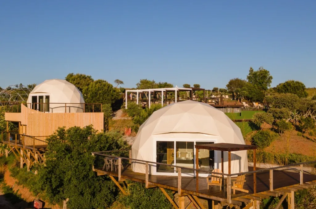 Image of two white glamping domes with spacious terraces and outdoor chairs, surrounded by trees