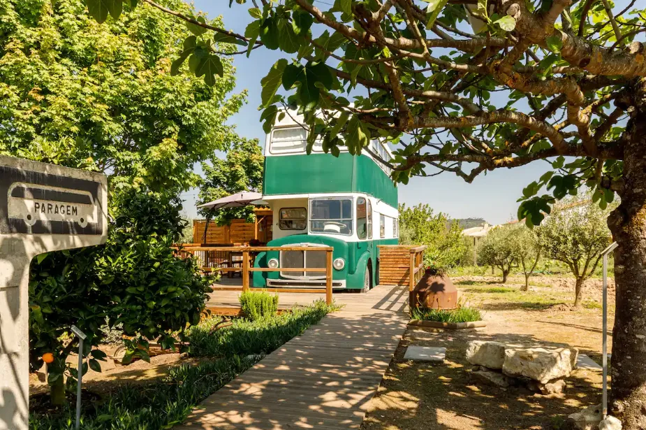 Image of a green and white retro bus parked in front of a wooden deck and surrounded by trees