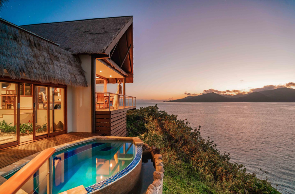 Image of a resort villa with a plunge pool and a terrace seen on the left, and the ocean on the right, taken at dusk