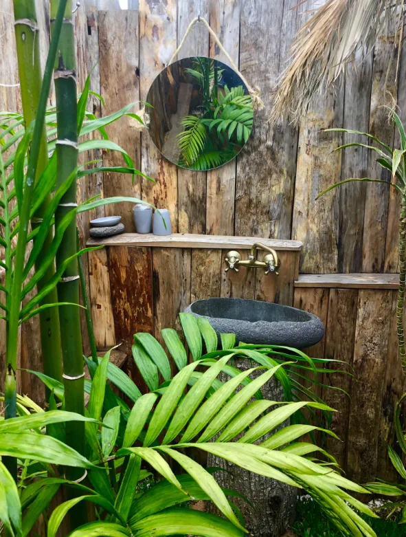 Image of a lavatory set on a wall made of wood boards, and surrounded by green foliage