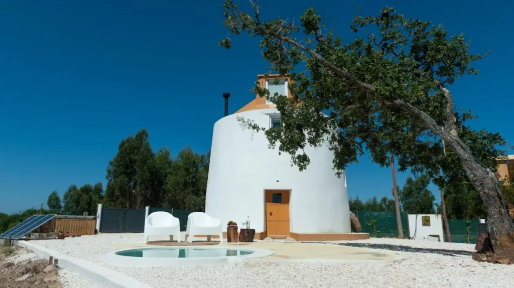 Image of a white and orange restored windmill, with a small plunge pool and two white chairs near the entrance 