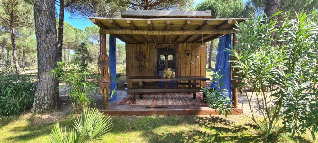 Image of a wooden cabin with an outdoor covered deck and a dining table, surrounded by trees