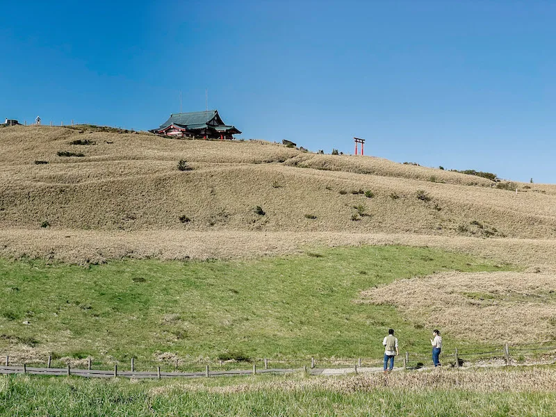 Two people standing on a trail, completely surrounded by countryside and a hill 