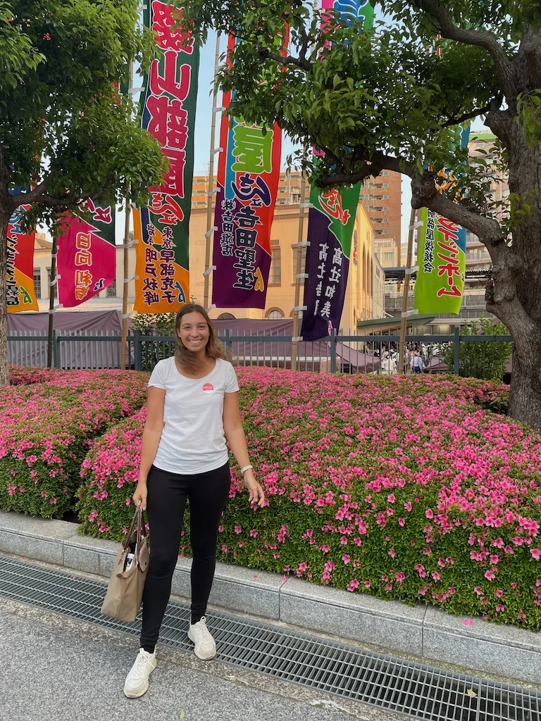 A woman in a white t-shirt and black pants posing in front of a bed of pink flowers in Tokyo