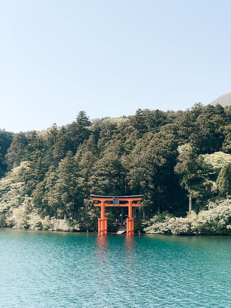 A Japanese red gate on the shores of a lake, with lush vegetation in the background