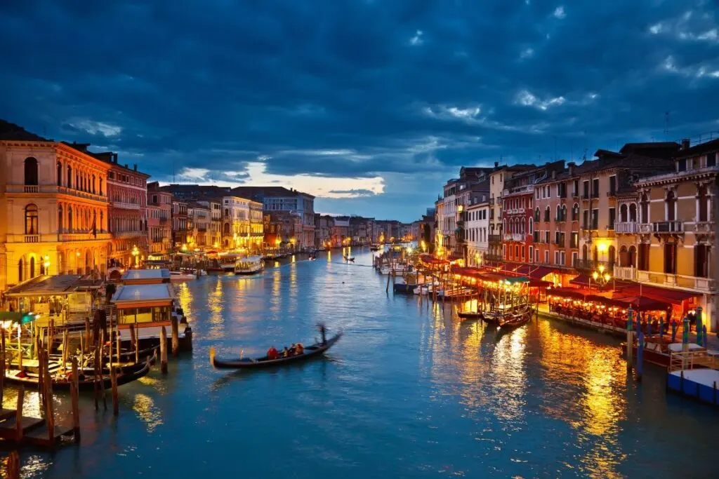 A Venice Canal at night, lined with lit-up buildings and anchored boats on both sides