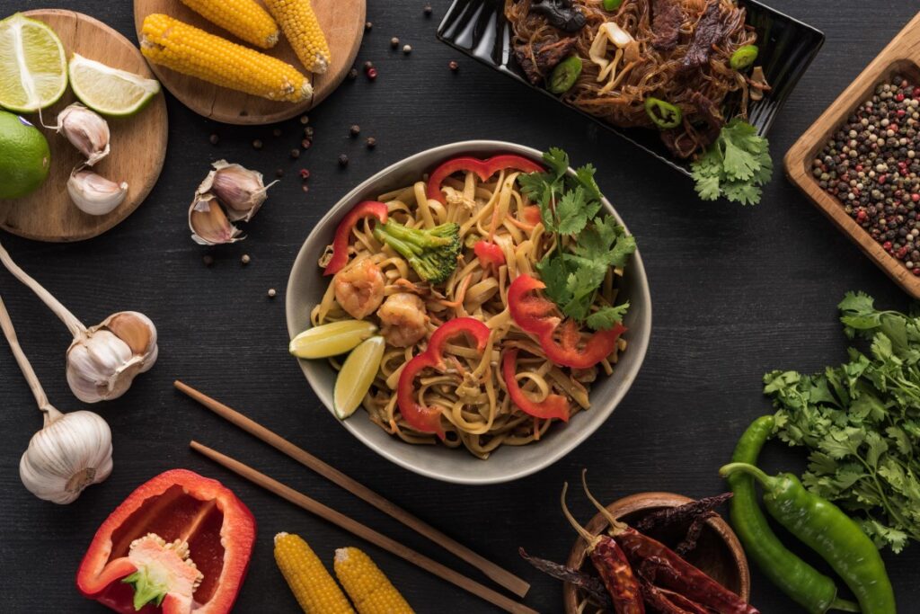 Image of a bowl of Pad Thai seen from above, placed on a black surfaces and surrounded by ingredients, inserted in a post about the best Bangkok Cooking Classes