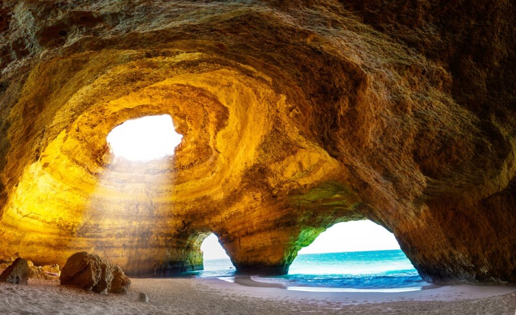 Photo of Benagil Cave in Portugal, with no people and sunlight pouring in from the opening in the ceiling