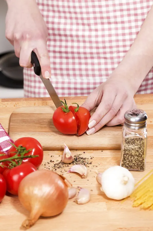 Hands chopping a tomato on a wooden board