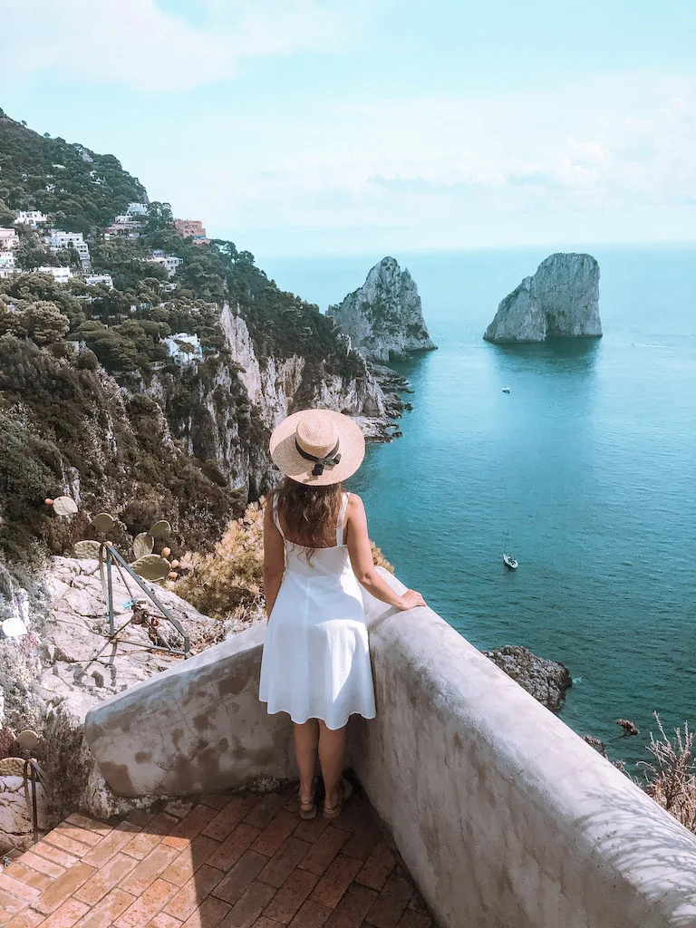 Woman from the back looking at the Faraglioni in Capri, one of the best ideas for a day trips from Naples.