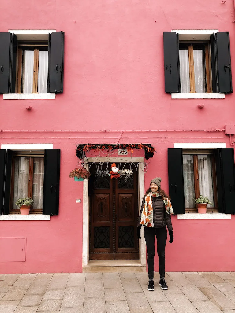 A girl standing in front of a pink building in Burano 