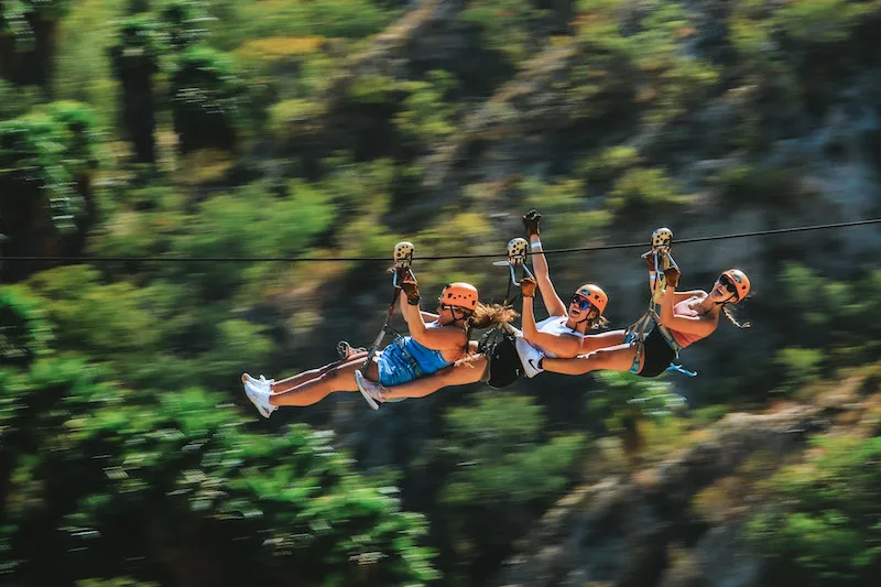 3 women with orange helmets ziplining in a line.