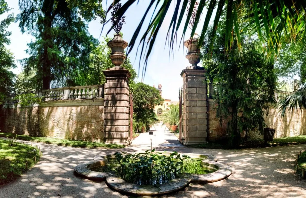 Entrance to the Botanical Garden of Padua, with a small pond with vegetation at the front and lush greenery