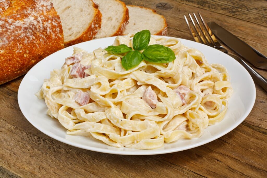 Tagliatelle Carbonara served on a white plate with bread slices on the side, a perfect dish to enjoy on a Florence to Pisa Day Trip 