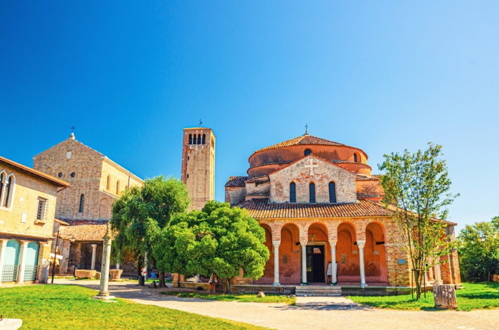 Church of Santa Fosca seen from the front on the island of Torcello, and the Church of Santa Maria Assunta with its bell tower to the left. Photo taken on a clear day with blue skies