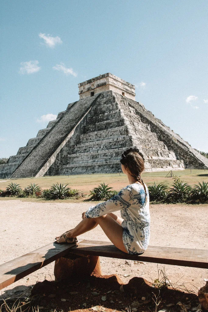 Woman sitting on a wooden in front of the Kukulkan pyramid at Chichen Itza.