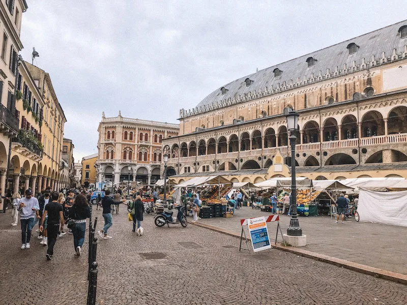 Piazza delle Erbe, bustling with visitors and the white tents of a local market 