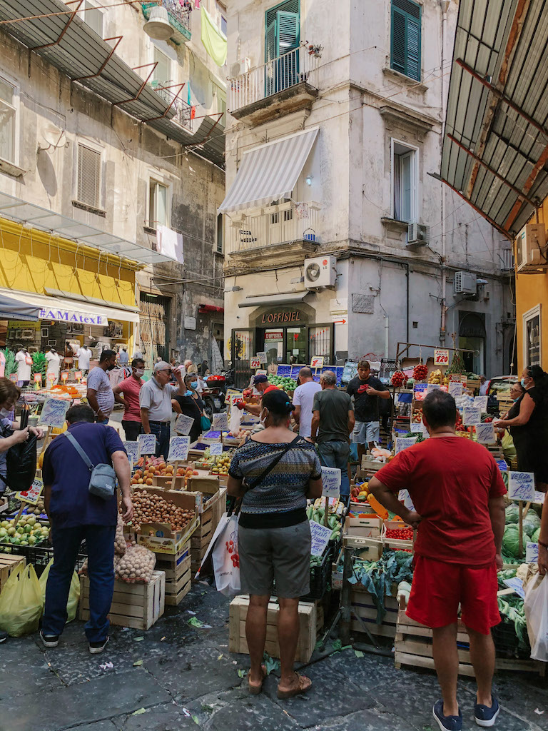 A local food market in Quartieri Spagnoli, Naples, with people standing around the stalls