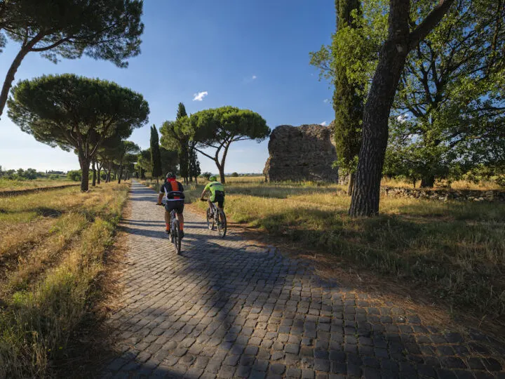 Image of two men cycling on the Appian Way in Rome, inserted in a post about the best Rome bike tours