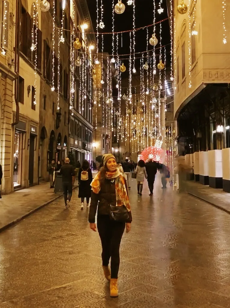 Image of a woman walking at night in Florence in a street decorated with Christmas lights